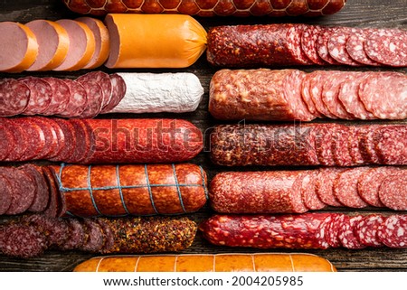 Set of different types of sausages, salami and smoked meat with basil and spices on wooden background. Top view.