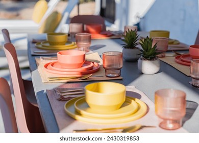 Set dining table outdoors with colorful bowls, plates, glasses, and silverware - Powered by Shutterstock