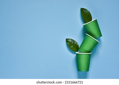 Set Of Eco-friendly Coffee To Go Cups - Green Kraft Paper Cups With Green Leaves Above On A Light Blue Background. Recycled Kraft Paper Packaging And Zero Waste Concept, Mockup. Top View, Copy Space 