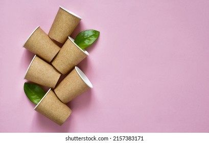 Set Of Eco-friendly Coffee To Go Cups - Kraft Paper Cups With Green Leaves Above On A Pink Background. Recycled Kraft Paper Packaging And Zero Waste Concept, Mockup. Top View, Copy Space