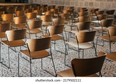 Set Of Empty Wooden Chairs Lined Up Before An Event In An Ancient Church Or Castle With Medieval Floor And Walls. Selective Focus.