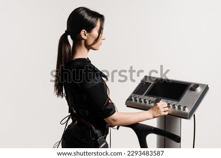 Set up EMS device for workout sport training in electrical muscle stimulation suit on white background. Girl trainer is setting up EMS device before training