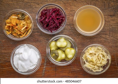 a set of fermented food great for gut health - top view of glass bowls against wood:  kimchi, red beets, apple cider vinegar, coconut milk yogurt, cucumber pickles, sauerkraut