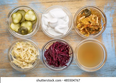 a set of fermented food great for gut health - top view of glass bowls against grunge wood:  cucumber pickles,  coconut milk yogurt, kimchi, sauerkraut, red beets, apple cider vinegar