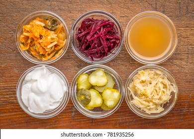 a set of fermented food great for gut health - top view of glass bowls against rustic wood:  kimchi, red beets, apple cider vinegar, coconut milk yogurt, cucumber pickles, sauerkraut