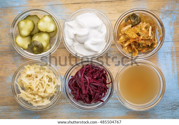 a set\
of fermented food great for gut health - top view of glass bowls\
against grunge wood:  cucumber pickles,  coconut milk yogurt,\
kimchi, sauerkraut, red beets, apple cider\
vinegar