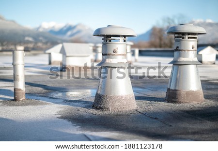 Set of flat roof vents on building with modified bitumen roofing system. Group of different shaped metal ventilators such as: bathrooms and laundry exhaust and plumbing stack vent. Selective focus.