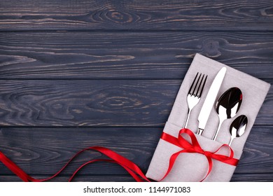 Set of fork, spoon, teaspoon and knife on linen napkin tied with red ribbon on wooden table. Top view.