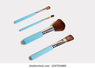 A set of four makeup brushes of different shapes on a white background. Four blue makeup brushes in different shapes and sizes. Fashionable women's beauty products to create beauty