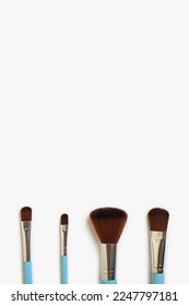 A set of four makeup brushes of different shapes on a white background. Four blue makeup brushes in different shapes and sizes. Fashionable women's cosmetics to create beauty. Free space for text