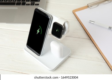Set of gadgets charging with wireless device on white wooden table