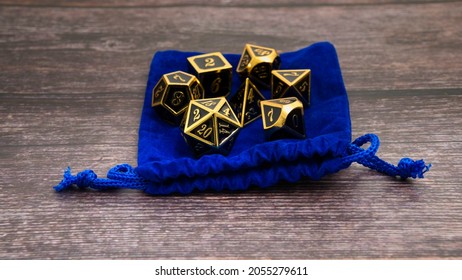 A Set of Gold and Black Metal Polyhedral Dice Sitting on a Blue Bag. Shallow Depth of Field.