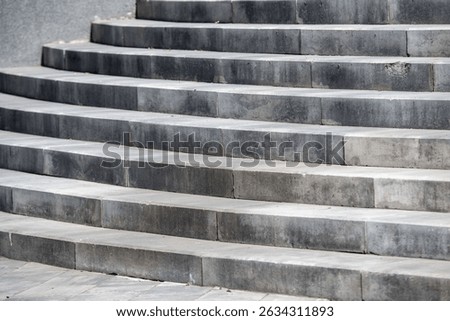 A set of gray steps that are worn and weathered. The steps are made of concrete and are arranged in a staircase pattern. The steps are not very noticeable, as they blend in with the background