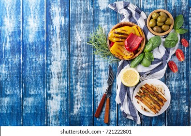 Set Of Greek Mezze: Grilled Halloumi Cheese, Pita Bread, Grilled Bell Peppers, Green Olives And Feta With Greens Decorated With Herbs, Lemon And Olive Oil Over A Blue Wooden Board. Top View