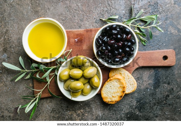 A set of Green and black olives and\
olive oil on a dark stone background, top\
view