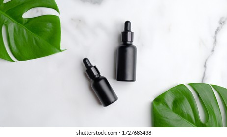 Set Of Hair Care Products On Marble Background. Natural Hair Lotion In Black Dropper Bottles With Monstera Leaf, Top View. 