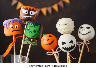 Set of Halloween treats on stick: Frankenstein, ghost, pumpkin; mummy on dark background.