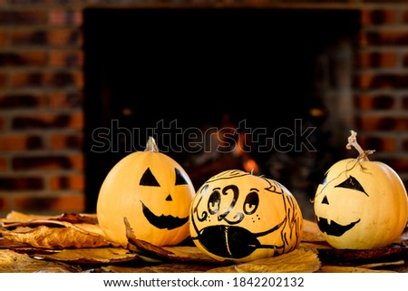 Set of hand painted Halloween pumpkins on a wooden table with autumn leaves and a fireplace in the background