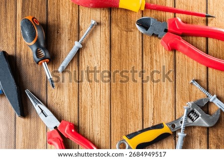 Set of hand tools including screwdrivers, pliers, wrench, hammer, and screws on wooden background. Top view.