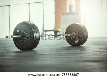 A set of heavy barbells sitting on a gym floor with a sun flare coming through the window 