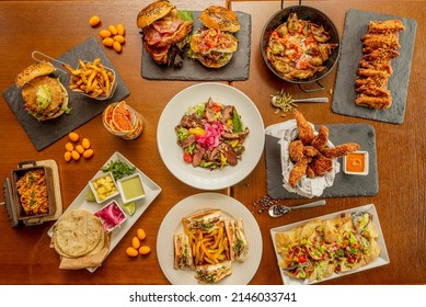 Set of homemade fast food dishes, sandwiches, Mexican al pastor tacos, burgers with fruits, quesadillas and nachos, barbecue wings, chicken fingers and salad with duck confit