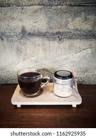 Set Of Hot Coffee (Caffe Americano) With Coffee Creamer In Glass Jar On Wooden Table Counter Bar With Grunge And Rough Concrete Wall Background In Cafe And Restaurant