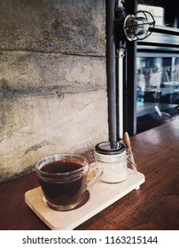 Set Of Hot Coffee (Caffe Americano) With Coffee Creamer In Glass Jar On Wooden Table Counter Bar With Grunge And Rough Concrete Wall Background In Cafe And Restaurant