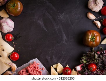 Set of ingredients for italian lasagna. Black food background with free space for text. Pasta, tomatoes, fresh ground meat, parmesan, mozzarella, basil, garlic on a rustic chalkboard. Overhead