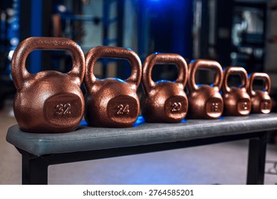 Set of kettlebells of different weights on bench in gym, strength training equipment lineup