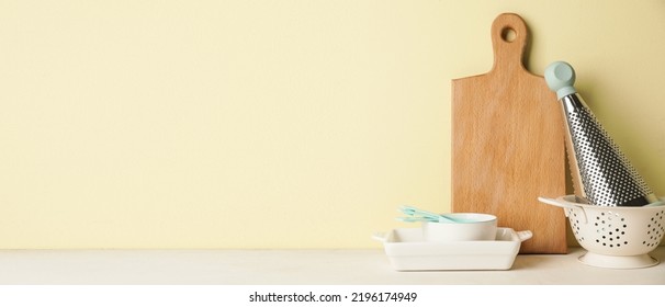 Set of kitchen utensils on table against yellow background with space for text