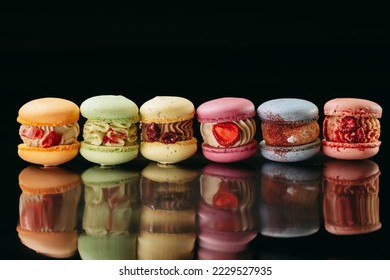 A set of large macaroons of different colors and different fillings. On a black isolated background. Macaroons in a row.