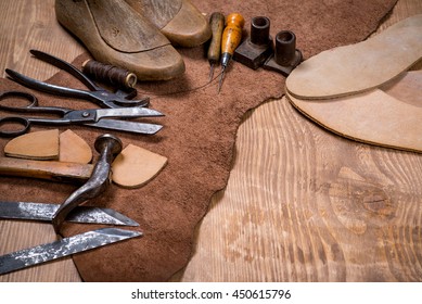 Set of leather craft tools on wooden background. Workplace for shoemaker. Piece of hide and working handmade tools on a work table. - Powered by Shutterstock