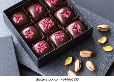 Set of luxury handmade bonbons with freeze-dried raspberry and pistachio in a gift box on black background. Exclusive chocolate candies