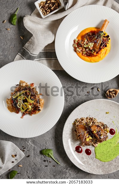 Set with main courses. Composition with meat dishes\
on gray stone table and textile in contemporary style. Roasted beef\
tongue with pearl barley; beef cheeks and leg of lamb in restaurant\
menu