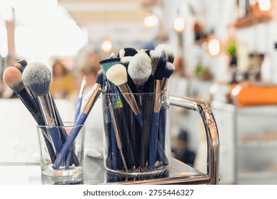 Set of makeup brushes on dressing table in beauty salon. Glass containers filled with various makeup brushes on salon trolley in beauty studio