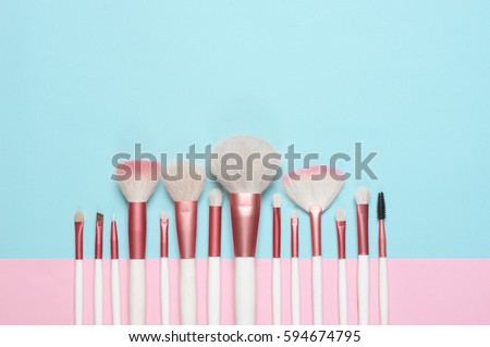 Set of makeup brushes on pink and aqua colored composed background. Top view point, flat lay.