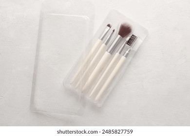 Set of makeup brushes in plastic box on a white concrete background