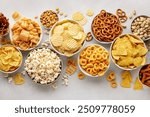 Set of many bowl with different salty snacks on light gray background. Chips, popcorn, nuts, nachos and pretzels. Party food. Top view