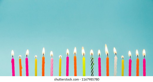 Set of many different color shape and pattern birthday candles burning isolated on blue. Happy Birthday card design concept.  Bottom lower border edge a lot of copy space.