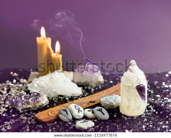 Set of many different psychic things on black\
background. Amethyst crystal pendulum, hand made rune stones,\
burning beeswax candles, crystal clusters, smoking incense.\
Spiritual healer concept.
