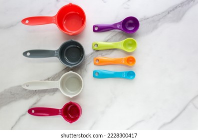 Set of measuring spoons and measuring cup made from colorful plastic lay on marble background.