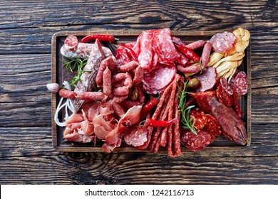 set of meat appetizer - jamon, chistorra, chorizo, salchichon, fuet, olives, tomatoes, chili peppers on a platter on a wooden cutting board on an old rustic table, horizontal view from above - Shutterstock ID 1242116713