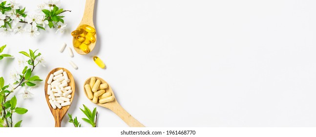 Set of medical capsules with probiotics, omega oils and multivitamins in the wooden spoons with blooming cherry branches on white background. Immunity support supplements. Health care concept. - Shutterstock ID 1961468770