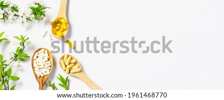 Set of medical capsules with probiotics, omega oils and multivitamins in the wooden spoons with blooming cherry branches on white background. Immunity support supplements. Health care concept.