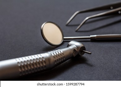 Set of metal dental instruments for dental treatment. High-speed dental handpiece, dental mirror and tweezers on black background. Medical tools. Shallow depth of field. Focus on the bur.