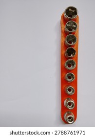 Set of metal socket wrench bits organized in a bright orange plastic holder, isolated on white