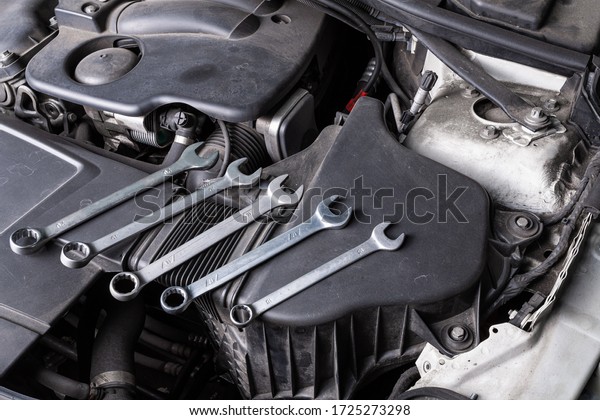 A set of metal spanners of different sizes lies\
under the hood of the car on an oil cooler. Concept of car repair\
and tools in car service