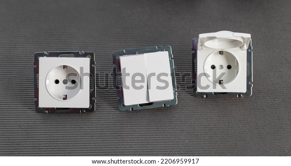 Set of modern electrical devices for the home.\
Electrical socket with a protective cover, a two-gang switch on a\
gray background