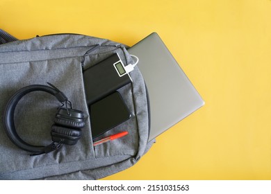 Set of modern gadgets: headphones, external battery, laptop and smartphone lie in a fashionable textile backpack. Yellow background. Travel and trip concept with gadgets. Copy space. Close-up