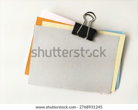 A set of multicolored paper notes are clipped together using a black binder clip. 